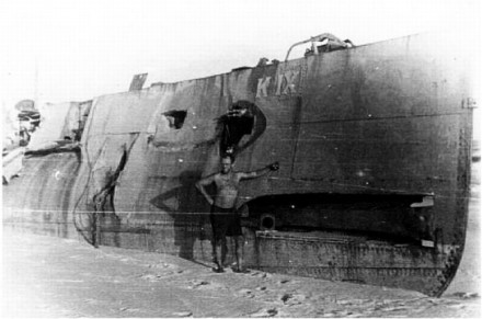A black and white photo of the submarine on the beach with a man in front of it.
