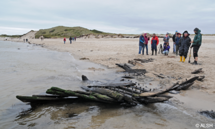 A photo of people near the remains of a wreck at a beach.