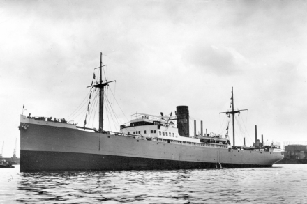 A black and white photo of the ship in a port, seen from the port side.