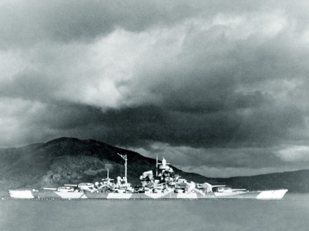A black and white photo of the Tirpitz in a fjord, in camouflage colours.