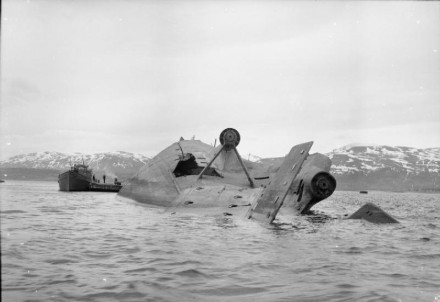A black and white photo of the hull of the Tirpitz lying upside down in the wate with a hole her side.