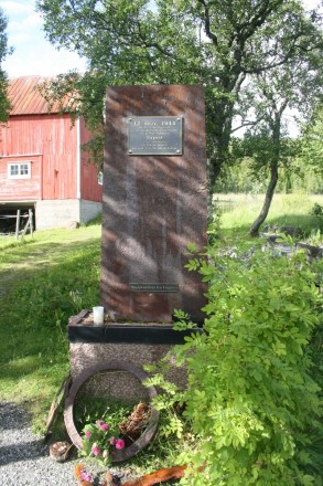 A photo showing a stone monument with a barn in the background.
