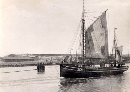 A black and white photo of the ship under sail in or near a port.