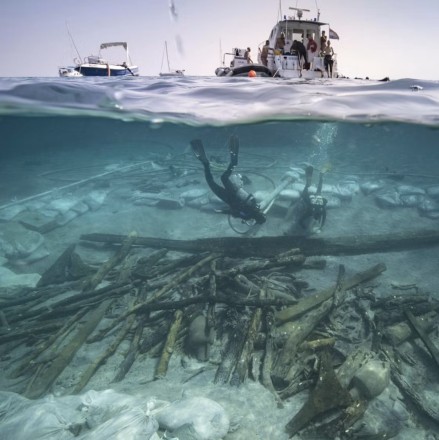 A photo, half above and half under water, showing a diver, ships and objects on the seabed.
